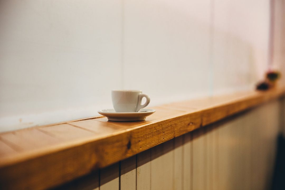 Eine Espressotasse auf der hölzernen Fensterbank vor einer hellen, sonnigen Wand