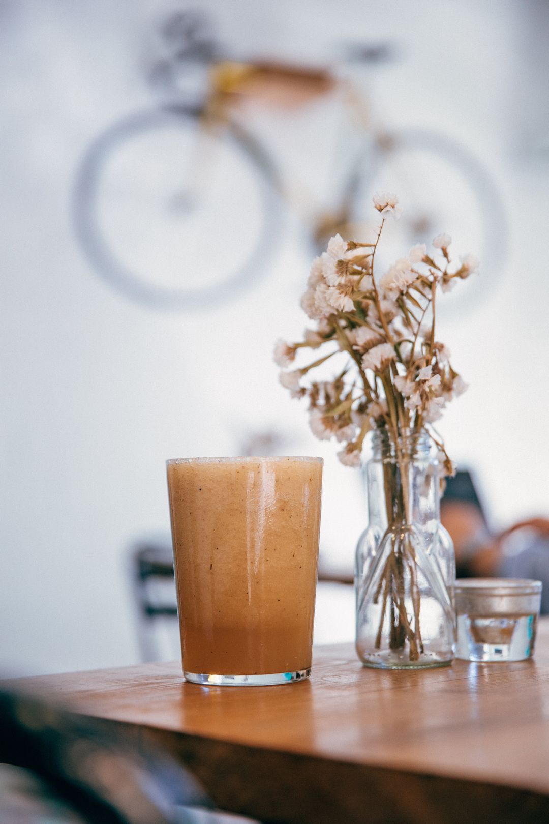 Ein Smoothie im Glas und eine kleine Vase mit Trockenblumen auf einem Holztisch