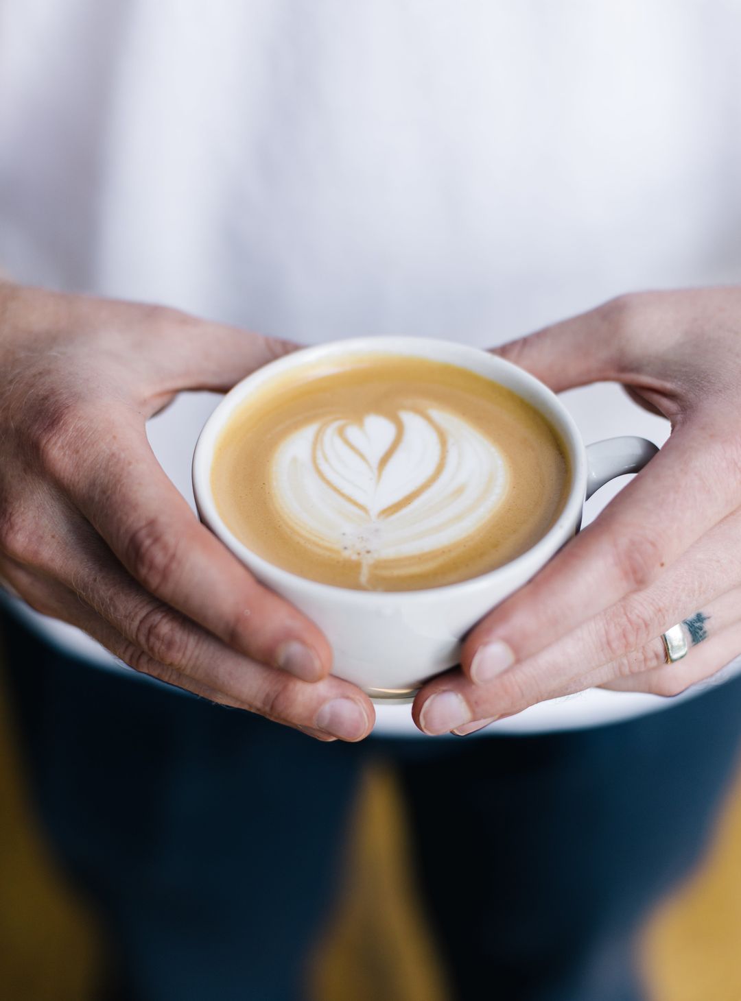Zwei Hände halten eine Tasse Cappuccino mit Milchschaum-Herz