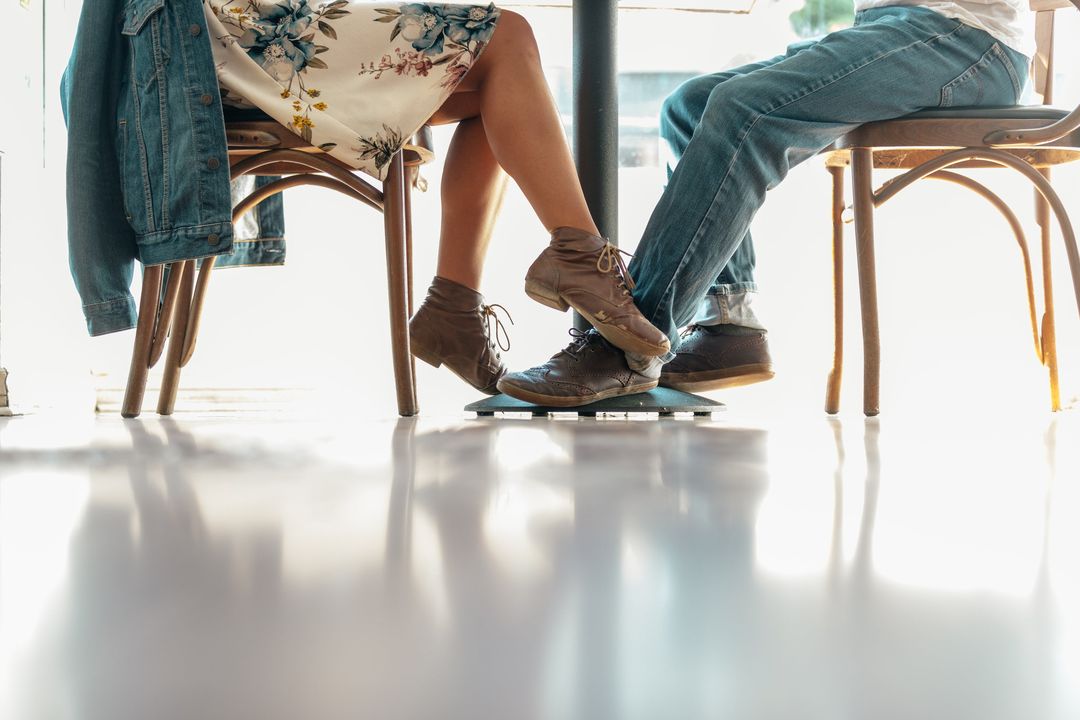 Zwei Gäste an einem Bistrotisch, man sieht nur Beine und Schuhe auf hellem Boden