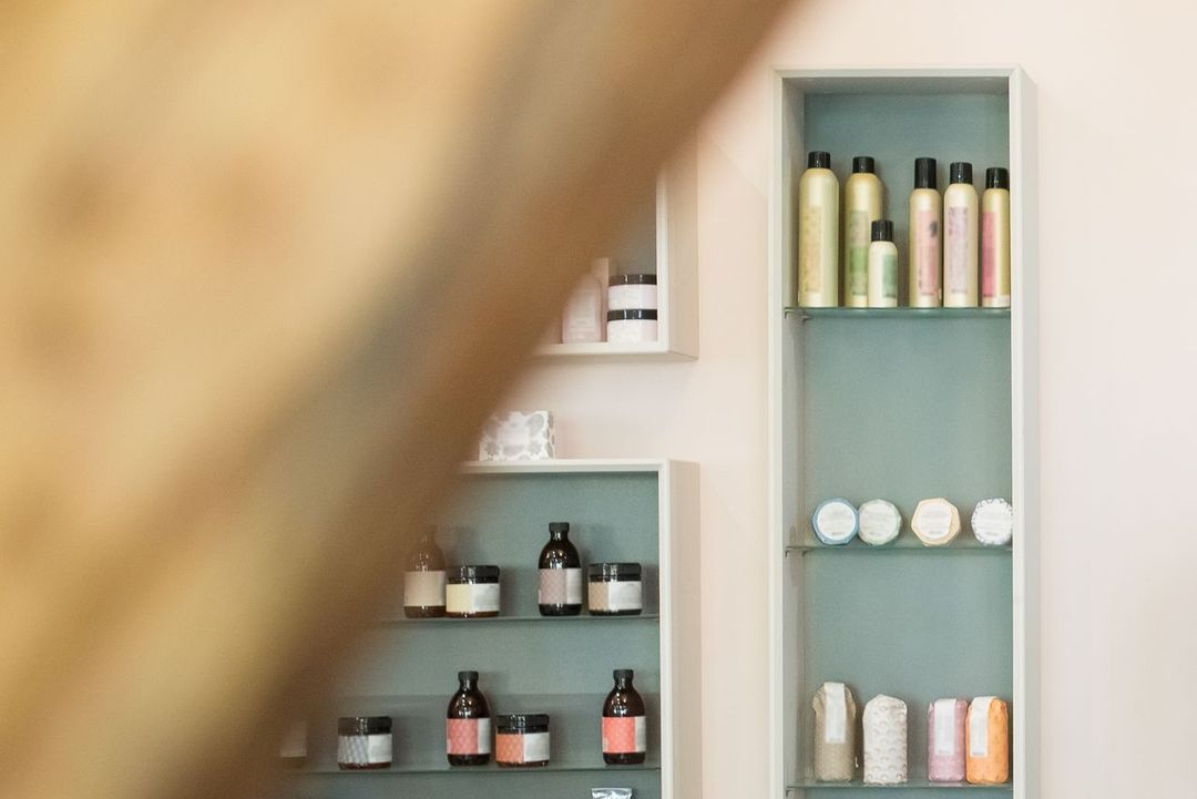 Empfang des Salons mit hellem Tresen, Regalen voller Pflegeprodukte und einer Vase mit Trockenblumen
