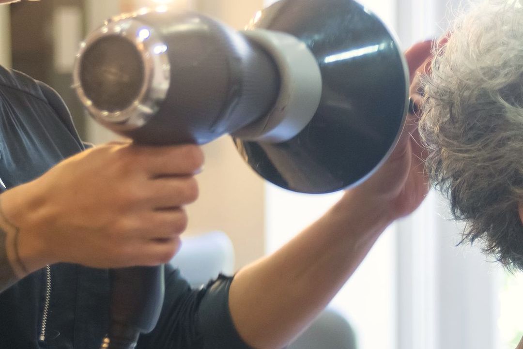 Die Friseurin föhnt einer lächelnden Kundin am hellen Fenster die Haare