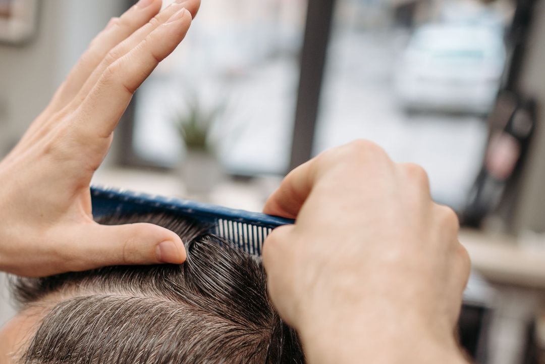 Ein Barbier zieht mit Kamm und Maschine die Seiten eines Herrenschnitts nach