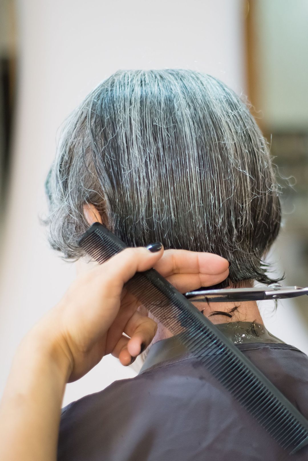 Mit Kamm und Schere wird das Haar im Nacken einer Kundin nachgeschnitten