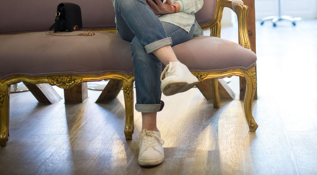 Eine Kundin wartet auf einem rosafarbenen Samtsofa mit goldenen Beinen und liest auf dem Handy