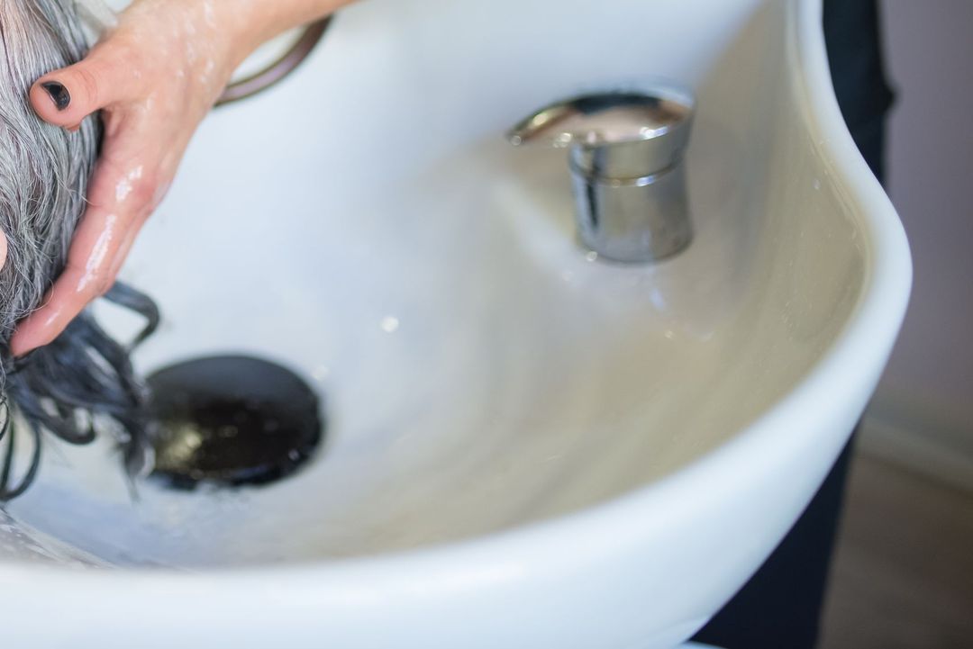 Eine Kundin liegt mit geschlossenen Augen am Waschbecken, ihr Haar wird gewaschen