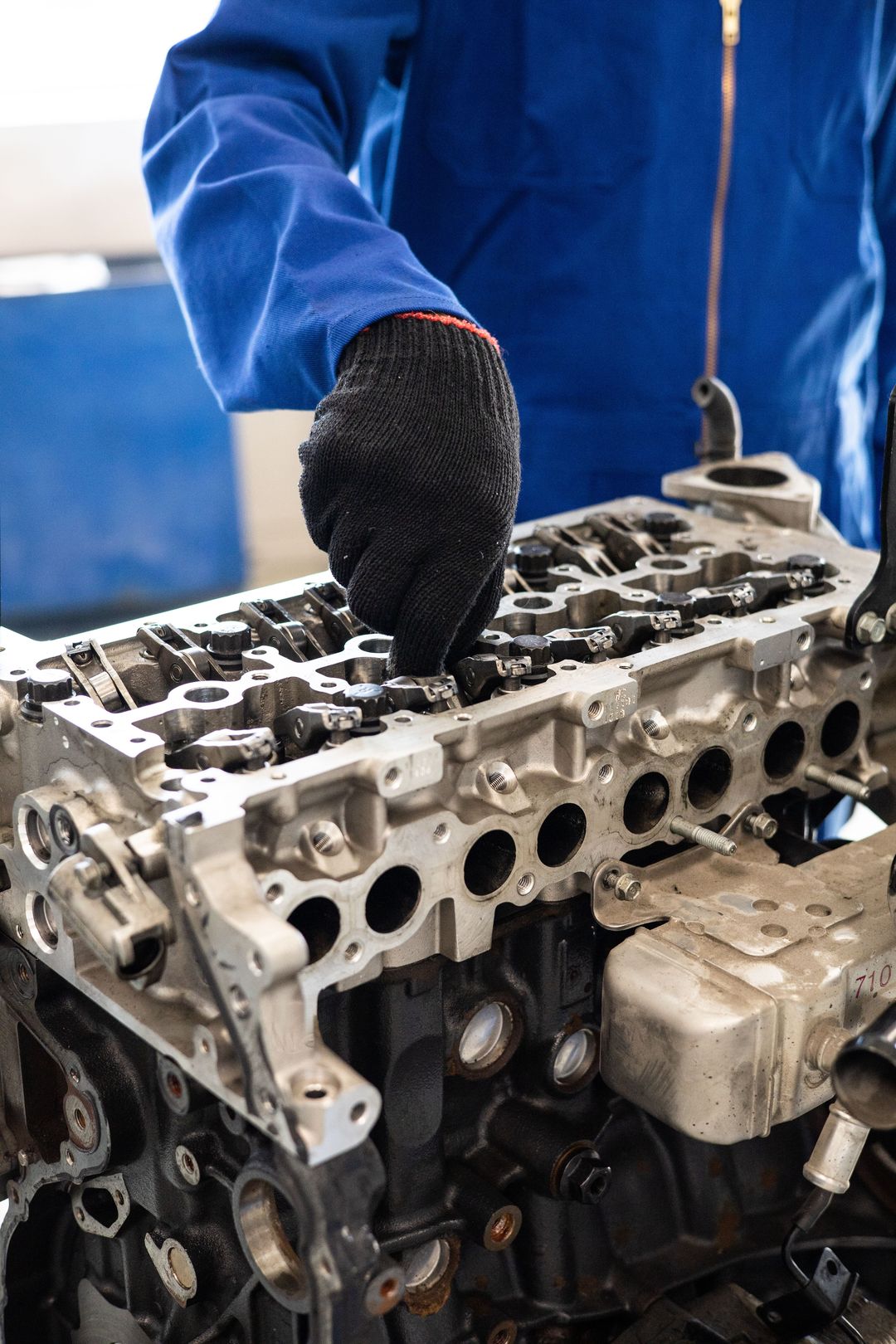 Eine Hand im Arbeitshandschuh an einem ausgebauten Motor, im Bild der blaue Overall