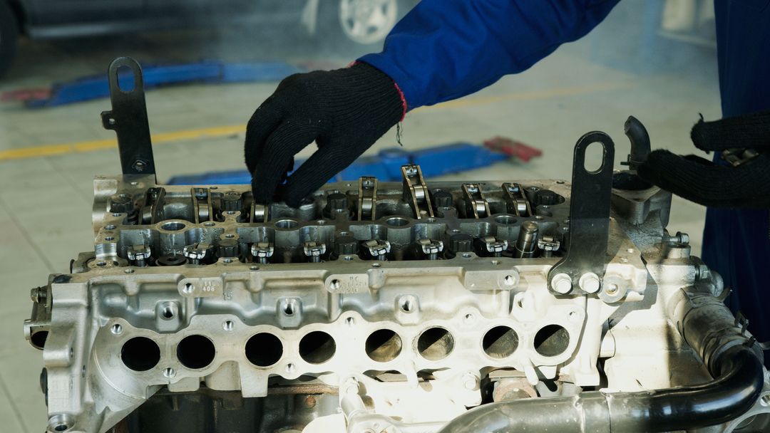 Zwei Hände in Arbeitshandschuhen am offenen Zylinderkopf eines Motors