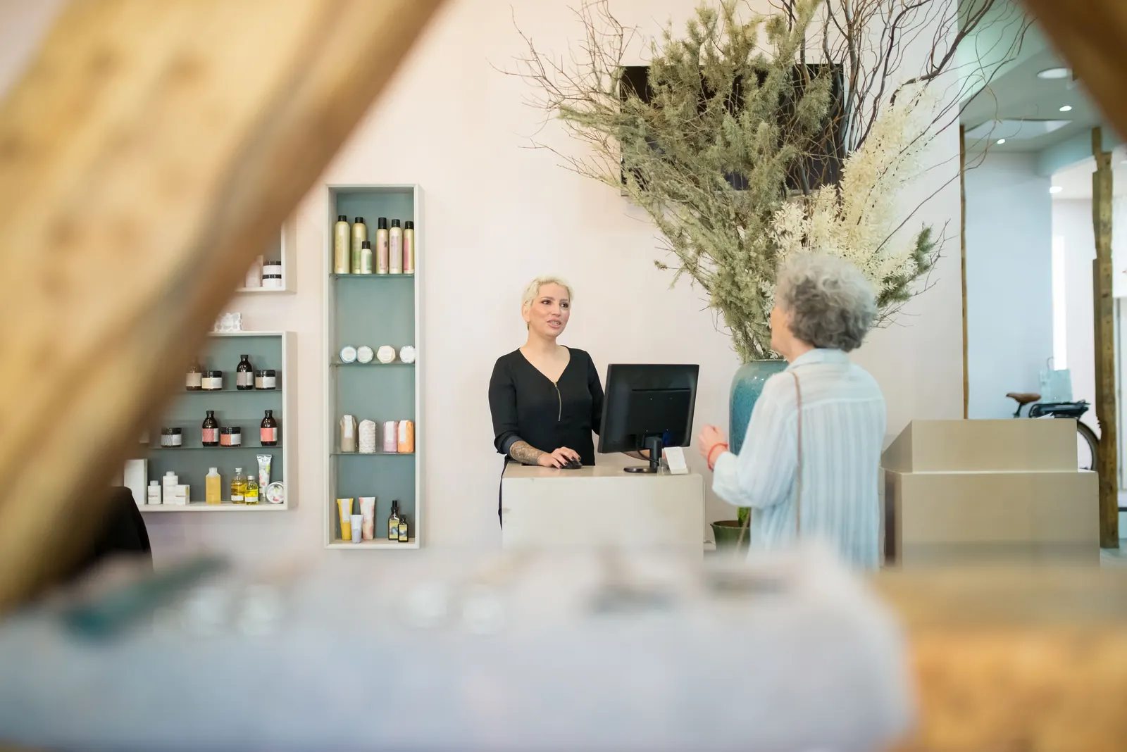 Eine Kundin kommt am Tresen eines kleinen Salons an, die Inhaberin begrüßt sie